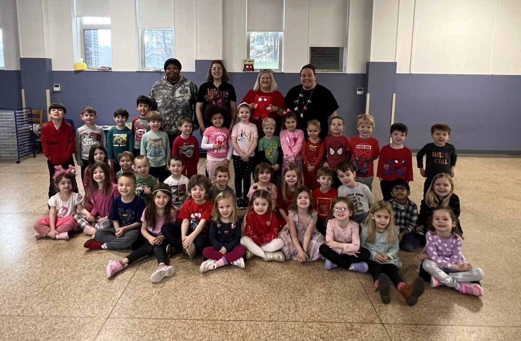 Teachers and children from a daycare center are gathered in a group smiling at the camera.