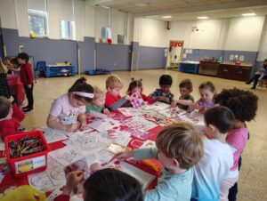 A group of toddlers and sit around a table doing arts and crafts.